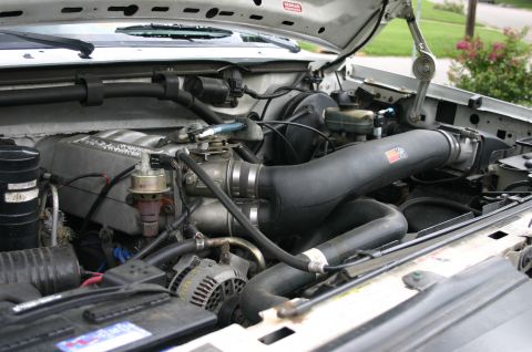 1994 Ford Bronco - Open engine bay of a silver Ford truck viewed from the driver's side, showing a black aftermarket cold-air intake tube running from the thr…
