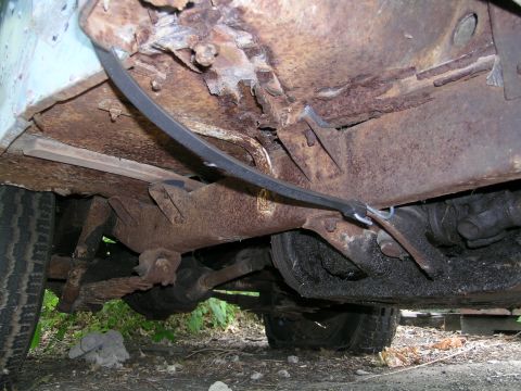 1950 Jeep CJ5 - The heavily corroded undercarriage of a vehicle, revealing rusted frame components, suspension parts, and tires.