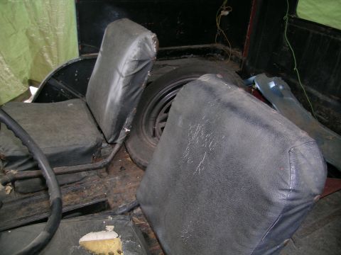 1950 Jeep CJ5 - The interior of a Jeep shows two seats, a spare tire, and the steering wheel, with some visible wear and tear.