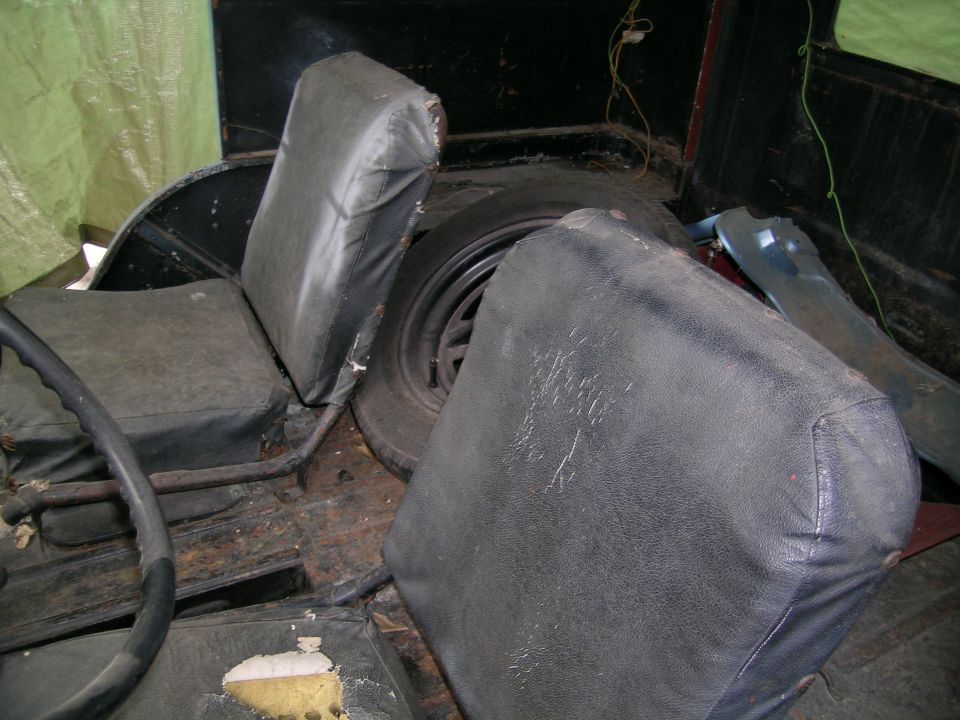 Worn black seat cushions and spare tire inside a rusty vintage vehicle interior