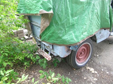 1950 Jeep CJ5 - A partially tarp-covered Jeep shows its rear bumper and a red-painted wheel.