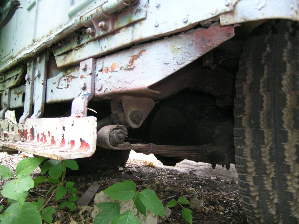 Underside of a pale green vintage 4x4 showing rusty leaf spring and running board