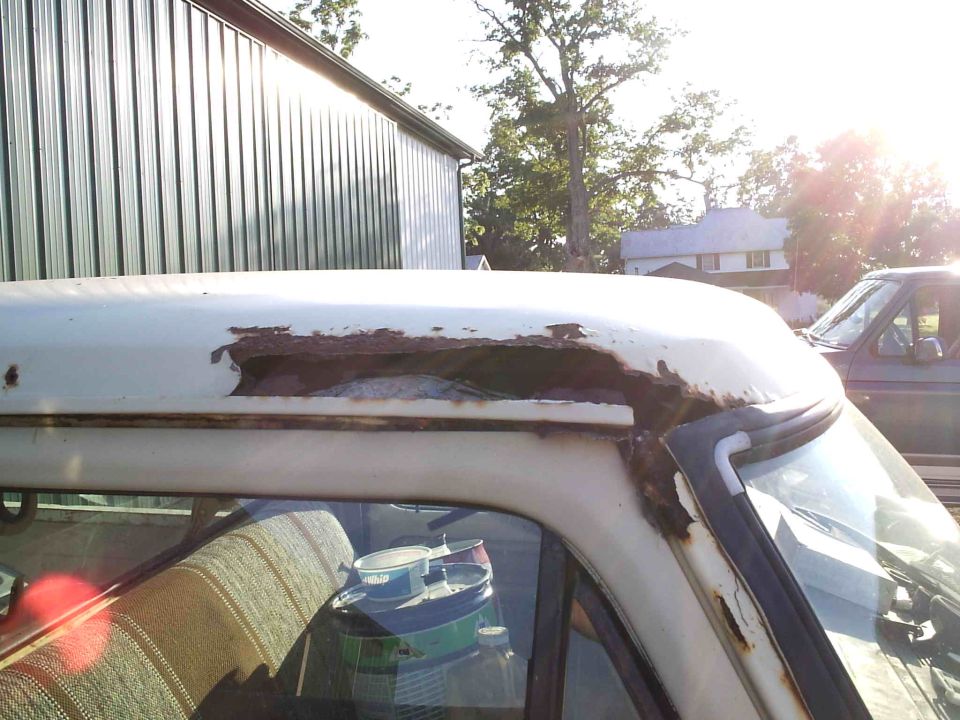 rusted roof edge of a white truck, another dark truck visible in background