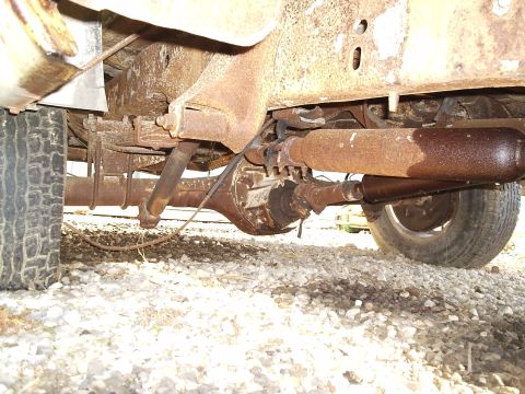 1979 Ford F-150 - The rear axle and exhaust components of a heavily rusted truck are visible from below.