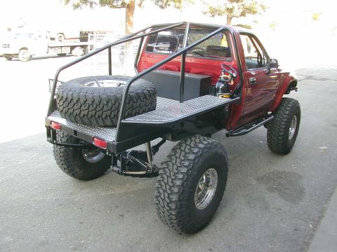1979 Ford F-150 - Three-quarter rear view of a lifted red pickup rock crawler with a fabricated diamond-plate flatbed, black exo/roll cage, tube rear bumper…