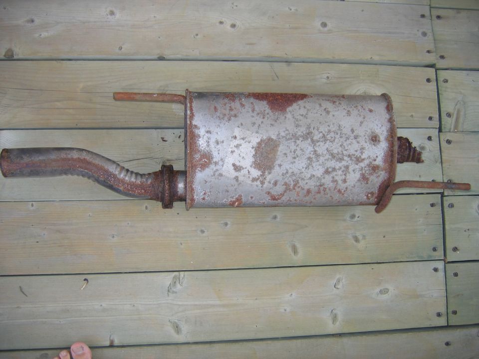 Rusty exhaust muffler with inlet pipe lying on wooden planks