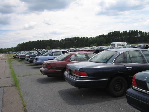 1991 Ford LTD Crown Victoria - A line of sedans are parked in an outdoor lot under a cloudy sky.