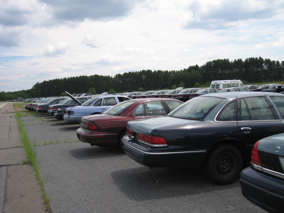 Cars parked in a lot, mostly sedans, with a white van in the background