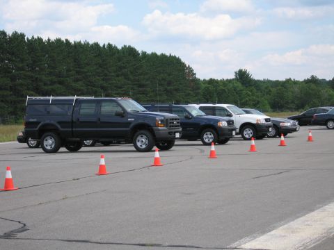 1991 Ford LTD Crown Victoria - A line of vehicles, including trucks and SUVs, are parked on an asphalt lot with traffic cones.