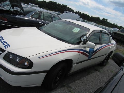 1991 Ford LTD Crown Victoria - A white police car is parked in an outdoor lot with other vehicles.
