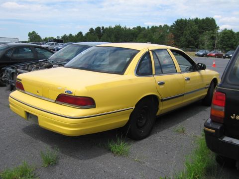 1991 Ford LTD Crown Victoria - A yellow sedan is parked in an outdoor lot, with other vehicles and trees in the background.