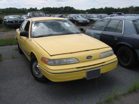 1991 Ford LTD Crown Victoria - A yellow 1991 Ford Crown Victoria LTD is parked in a junkyard with other vehicles.