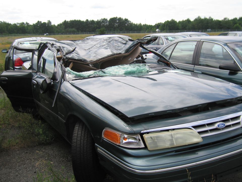 Front view of a wrecked 1991 Ford Crown Victoria LTD with a tarp over the collapsed roof and broken windshield