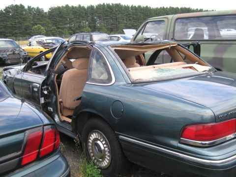 1991 Ford LTD Crown Victoria - This damaged sedan sits in a junkyard, its roof caved in and windows shattered.