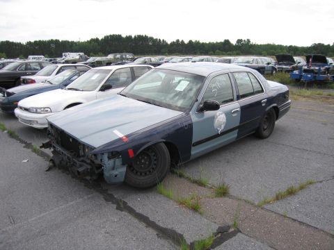 1991 Ford LTD Crown Victoria - A damaged police car sits in a lot with other vehicles under an overcast sky.