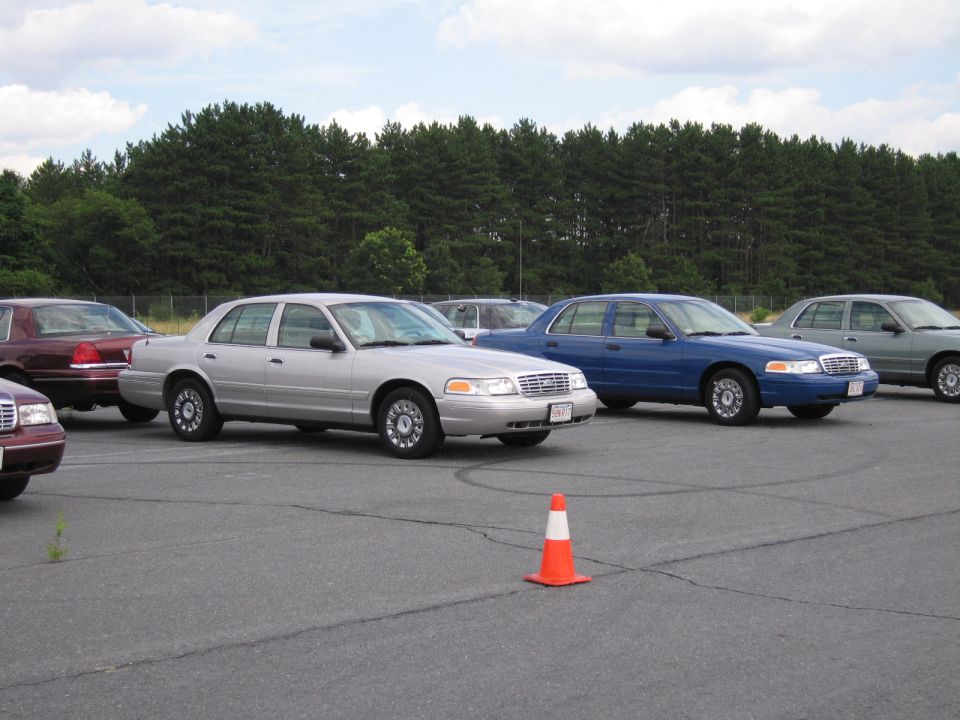 Several Ford Crown Victorias parked in a lot, one silver, one blue, and two darker ones in the background
