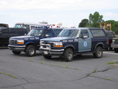 1991 Ford LTD Crown Victoria - Two state police SUVs are parked on asphalt, with an ambulance and other vehicles in the background.
