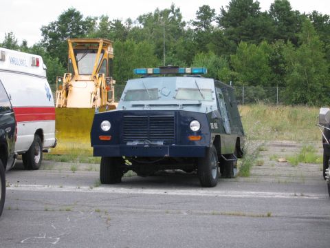 1991 Ford LTD Crown Victoria - An armored vehicle with emergency lights sits parked next to an ambulance and a construction vehicle.