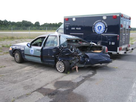 1991 Ford LTD Crown Victoria - A heavily damaged 1991 Ford Crown Victoria LTD police car sits next to a Massachusetts State Police ambulance, its trunk open and rear end…
