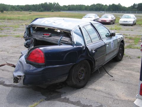 1991 Ford LTD Crown Victoria - A heavily damaged police car sits in a lot with other vehicles visible in the background.