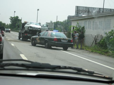 1991 Ford LTD Crown Victoria - A state police car and a tow truck are stopped on the side of the road next to a damaged white car.