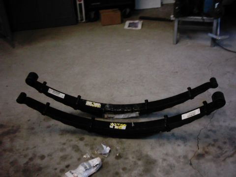 1978 Ford Bronco - Two leaf springs are laid out on a garage floor, likely for replacement or repair.