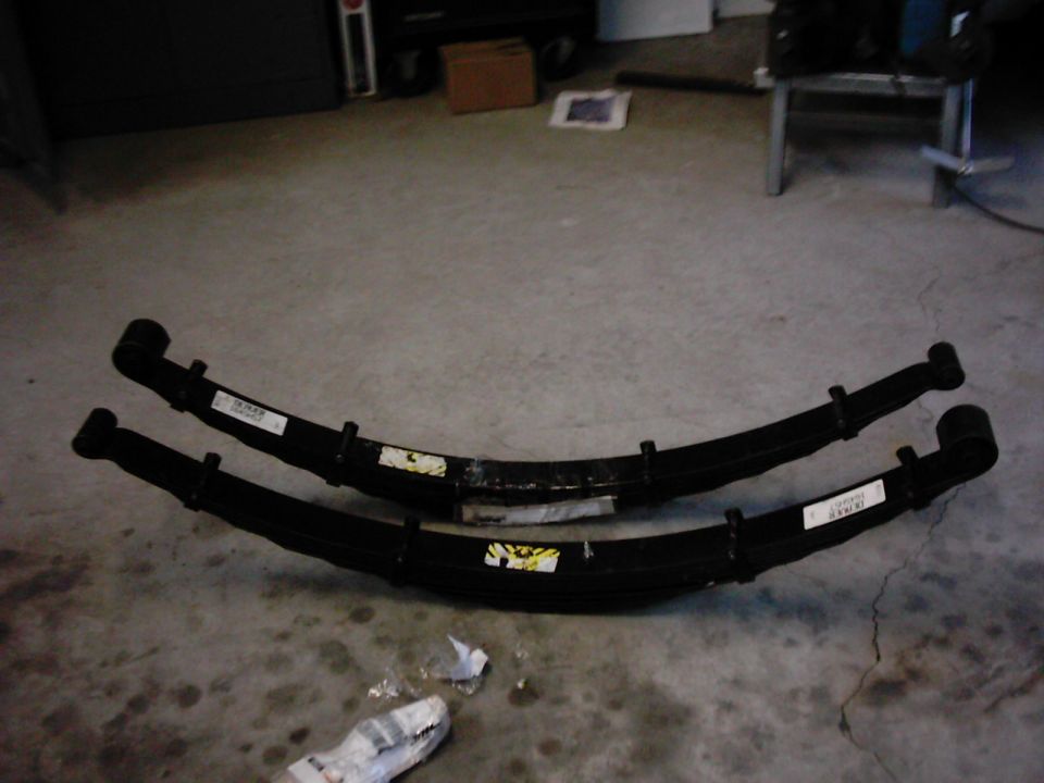 Two black leaf springs on a concrete floor. Labels are visible on both
