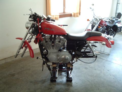 2002 Harley-Davidson Sportster Custom - A red 2002 Harley-Davidson Sportster Custom is shown on stands, with another motorcycle in the background.