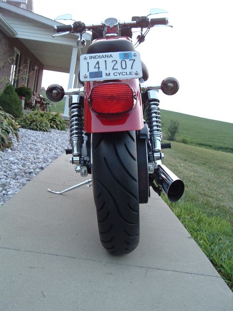 2002 Harley-Davidson Sportster Custom - A red motorcycle is parked on a sidewalk in front of a house, with a grassy hill in the background.