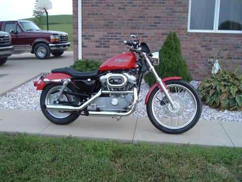 2002 Harley-Davidson Sportster Custom - A red Harley-Davidson motorcycle is parked on a driveway next to a brick building and a pickup truck.