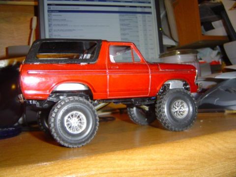 1979 Ford Bronco - A red toy Bronco model with a lifted suspension and large off-road tires sits on a wooden surface.