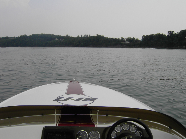 View from inside a boat looking forward at the water and shoreline. The boat has a steering wheel and gauges