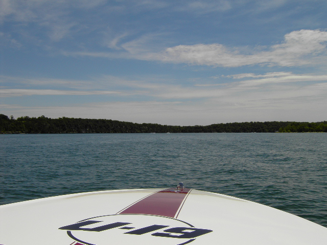 Bow of a white boat with a maroon stripe and blue lettering 'U-19'. Water and trees in the background