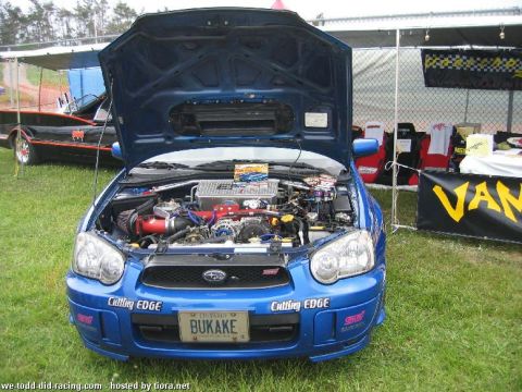 2000 Jeep Cherokee - A blue Subaru Impreza WRX STI is displayed with its hood open, revealing a modified engine bay and custom decals.