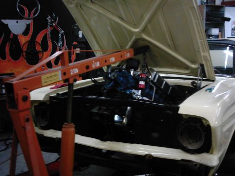 1978 Ford Bronco - An engine hoist is positioned over a car's engine bay, with the engine partially removed for service.