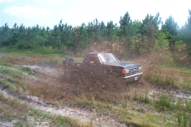 Dark pickup truck blasting through a muddy trail, mud spraying off the rear tires