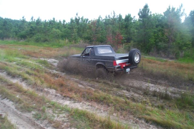 Black 1988 Ford Bronco stuck in mud, rear view with spare tire mounted