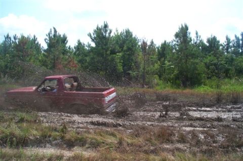 1988 Ford Bronco - A red pickup truck is stuck in the mud, with water splashing around it.