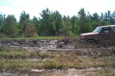 1988 Ford Bronco - Ford Bronco navigating a muddy terrain with trees lining the horizon.