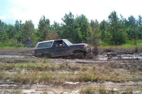 1988 Ford Bronco - A Ford Bronco navigates a muddy terrain with trees in the background.