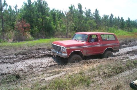 1988 Ford Bronco - A red SUV is stuck in a muddy field with trees in the background.