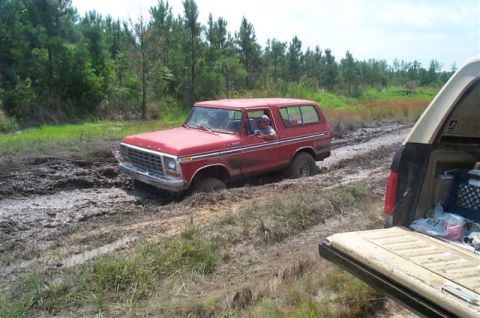 1988 Ford Bronco - A red 1978 Ford Bronco is stuck in a muddy track, with the tailgate of another vehicle in the foreground.