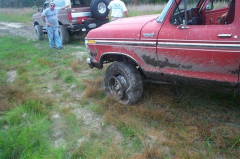 1988 Ford Bronco - Two Ford trucks stuck in mud, one with a flat tire.