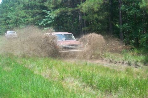 1988 Ford Bronco - A Ford Bronco navigates a muddy trail, sending dirt and water flying.