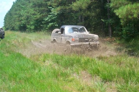 1988 Ford Bronco - A Ford Bronco navigates a muddy trail, kicking up dirt as it goes.