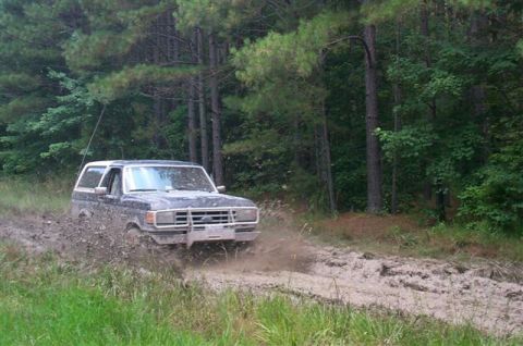 1988 Ford Bronco - A dark 1987 Ford Bronco navigates a muddy path through a dense forest.