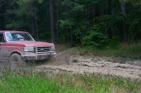 1988 Ford Bronco - Ford F-Series truck navigating a muddy off-road path surrounded by trees.
