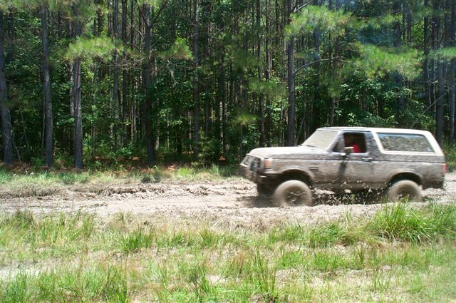 Mud-splattered Ford Bronco driving through a muddy track in a forest