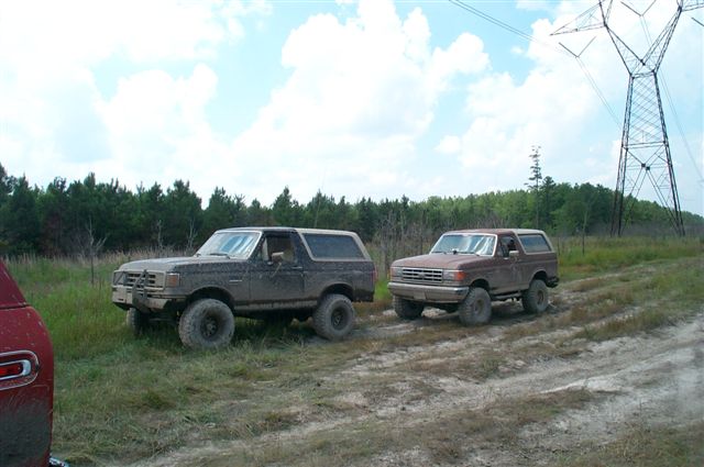 Two muddy 1988 Ford Broncos parked off-road near power lines
