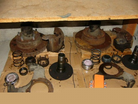 1995 Ford Bronco - Various rusty automotive brake and suspension components are spread out on a wooden surface.